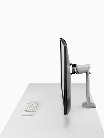 Silver single Flo X monitor arm with a 43'' screen, viewed from the side.