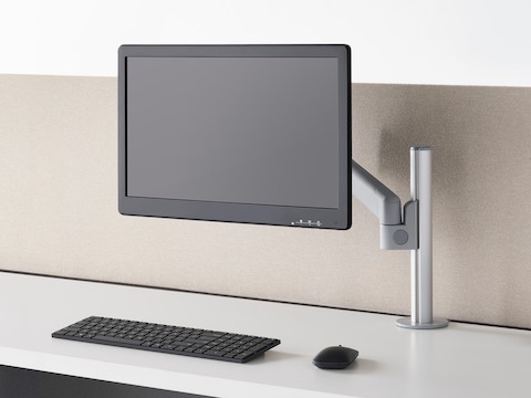 Three-quarter front view of a grey Lima Monitor Arm, on a sit-to-stand desk with a monitor and keyboard.
