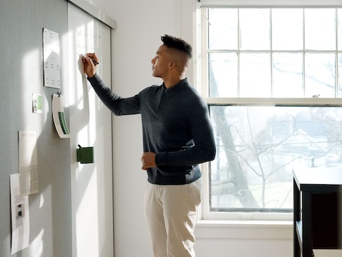 A man writes on a OE1 Wall Rail and Board marker board.