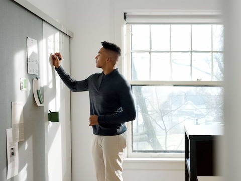 A man writes on a OE1 Wall Rail and Board marker board.