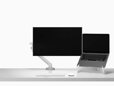 An open laptop raised on an Oripura Laptop Stand next to a monitor arm and screen on top of a worksurface