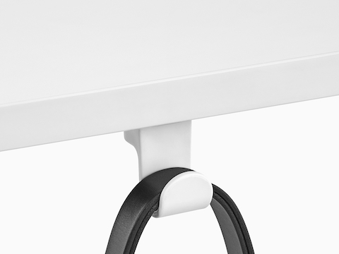 A black strap loops over a fixed Ubi Bag Hook affixed to the underside of a work surface.