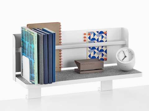 A Ubi Attached Shelf with a backdrop supports a small clock, hole punch, books, and other reference materials.
