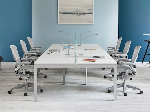 A white rectangular meeting table with three light grey Aeron office chairs on either side.
