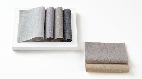 Multiple folded 100% recycled content fabric swatches in varying colors including neutrals, reds, greens, blues and purples.