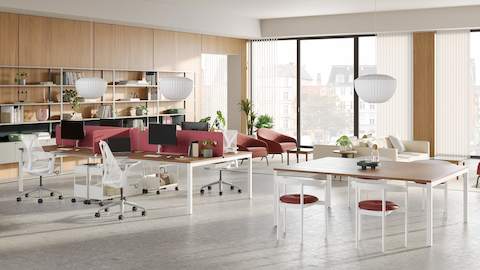 An office with open shelving along the back wall and options for dedicated workstations or team tables in the foreground. Additional ancillary seating areas are in the background.