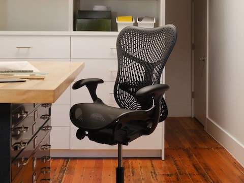 A Mirra 2 Stool with a TriFlex back and adjustable arms in graphite by a storage table in a design studio.