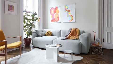 A Mags Sectional With Chase in grey by HAY sits in a room with artwork, bookshelves, and a HAY Tulou Coffee Table in green. 