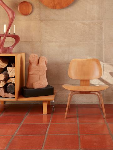 An Eames Moulded Plywood Lounge Chair with a wood base next to a scuplture.