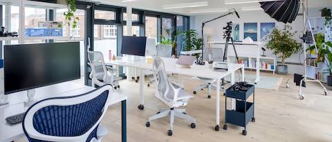 White OE1 mobile tables with mid-back Cosm chairs and a height-adjustable Ratio desk in the background.