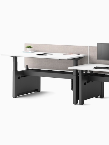 A cluster of four Ratio height-adjustable desks, positioned at seating and standing heights, attached side by side with framed, beige mounted privacy screens.