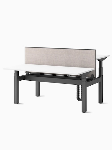 Two Ratio height-adjustable desks, positioned at seating and standing heights, back-to-back with a framed, beige mounted privacy screen.