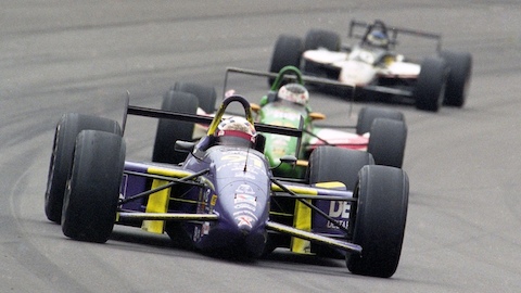 Three Indy cars turn the corner of a racetrack. Select to go to an article about the link between auto racing and Herman Miller work chairs.