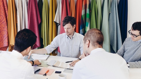 Four seated men review fabric samples.