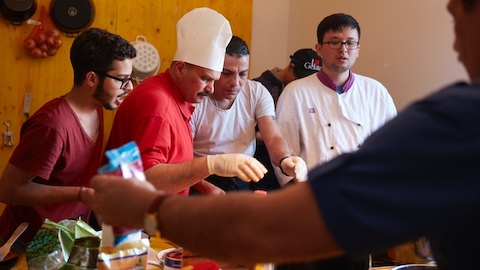 Four men interact while preparing food. Select to go to a WHY Magazine article featuring Vienna design firm EOOS.